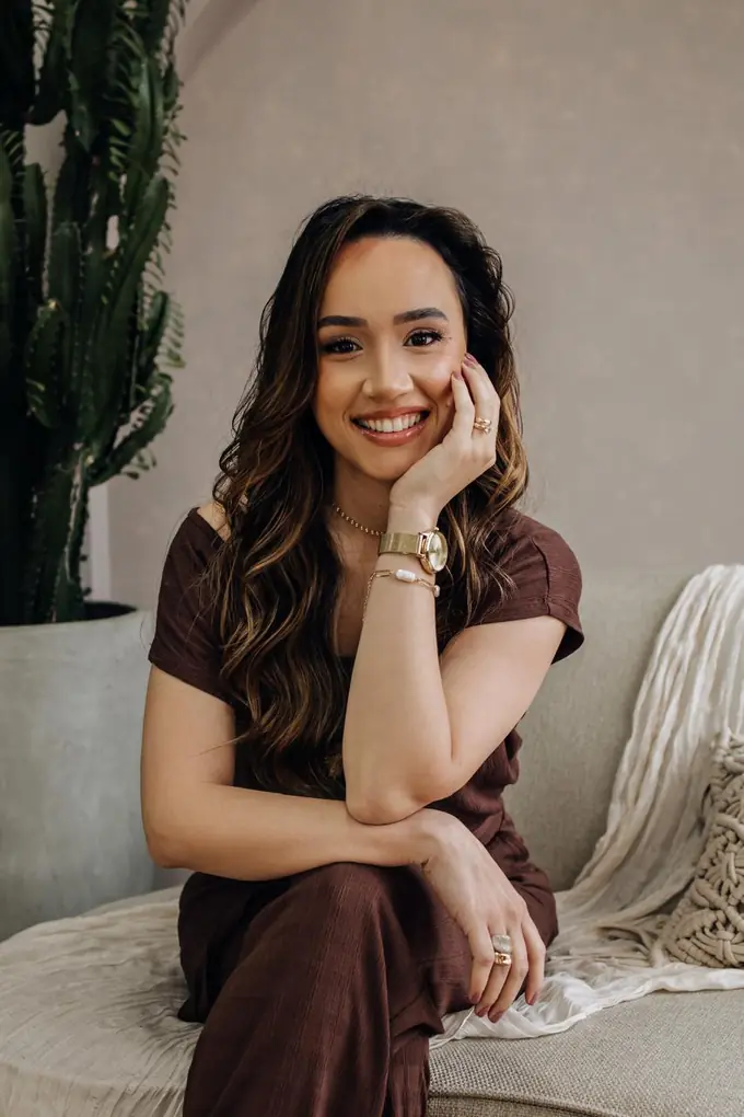 Talita Santos sentada em um sofá claro, sorrindo, com a mão apoiada no rosto